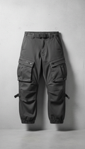 A pair of urban cargo pants is centered in the frame against a simple concrete wall. The lighting is soft and even,...