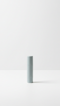 A sleek, portable SPF lip balm in Cool Grey from Urban Nomad is centered on a Cloud White surface. The product is...